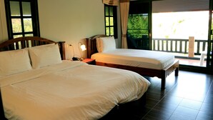 Habitación de hotel con dos camas, una mesita de noche, una lámpara y vistas al exterior a través de un ventanal corredero.