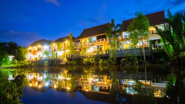 Un hotel frente al agua con varias edificaciones, un reflejo en el agua y un cielo nocturno.