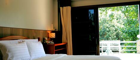 A bedroom with a bed, a nightstand with a lamp, and a view of a balcony with a white fence.
