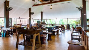 Amplio espacio interior con mesas y sillas de madera, ventiladores y un techo alto con vigas a la vista.