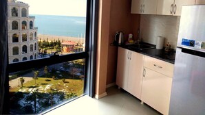 A kitchen with a view of a beach and a building with arched windows. - Rock Hotel First Line (Batumi)