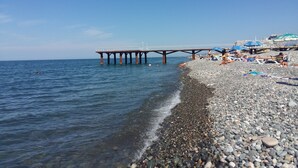 A pebbled beach with a pier extending into the sea. - Rock Hotel First Line (Batumi)