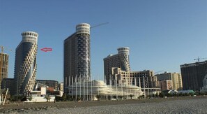 A modern urban skyline with several high-rise buildings, including a distinctive cylindrical structure and a building with a unique, layered facade. - Rock Hotel First Line (Batumi)