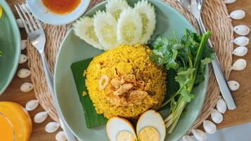 A table with a plate of yellow rice, boiled eggs, cucumber slices, and a coconut.