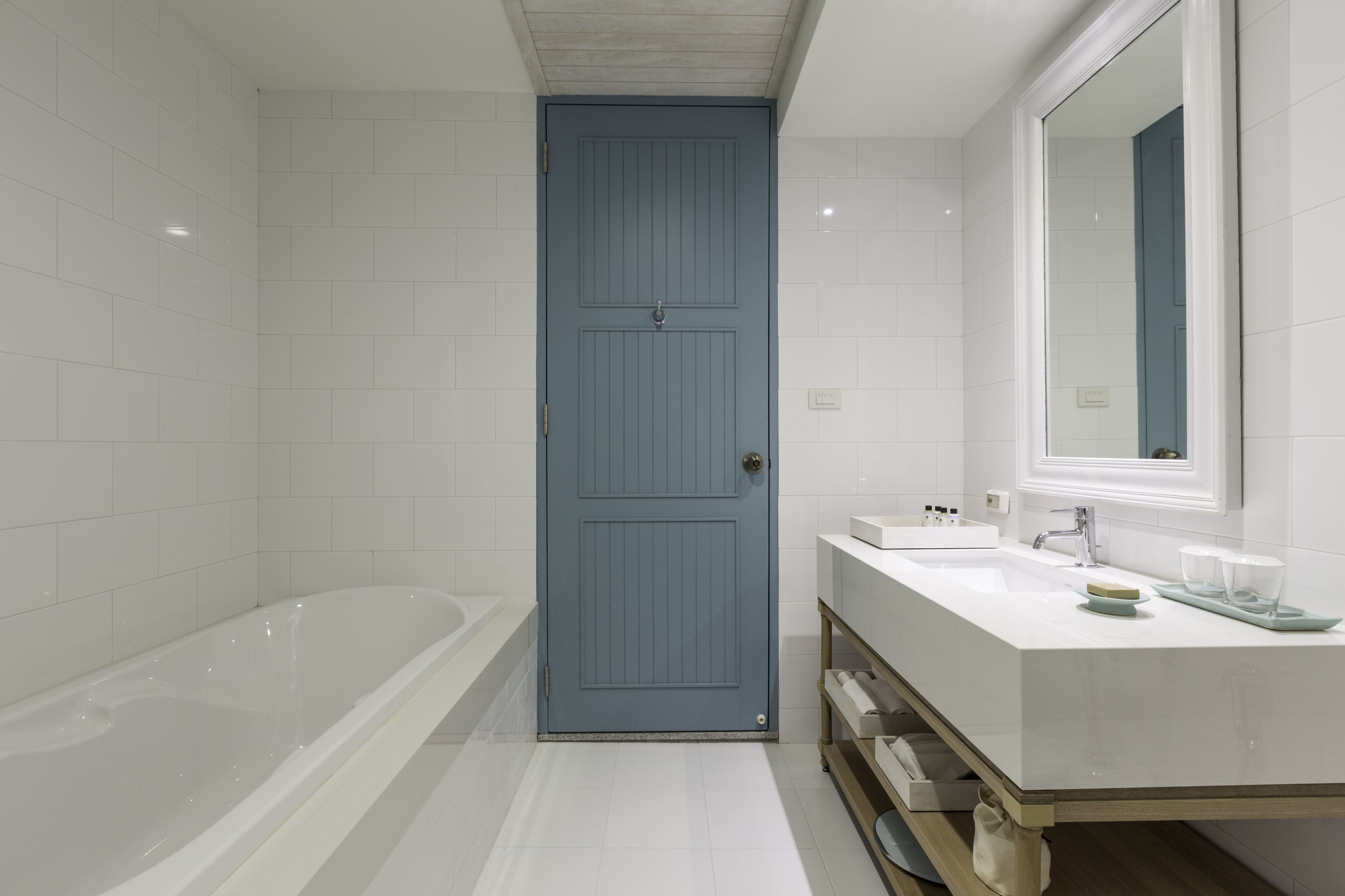 Un baño moderno con una bañera blanca, una puerta azul y un tocador blanco con espejo.