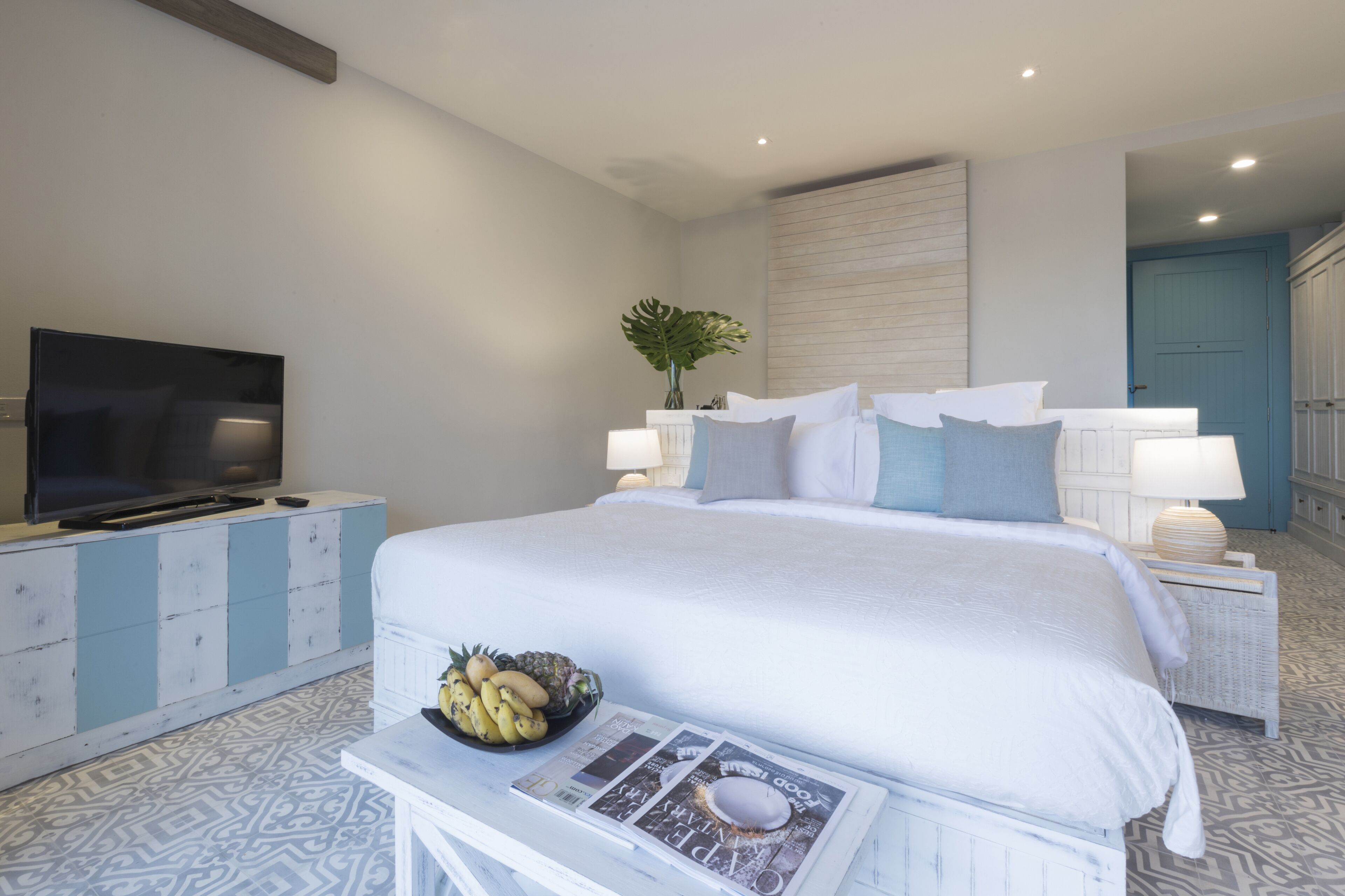 A modern bedroom with a large bed, a flat-screen TV, a bedside table with a bowl of fruit, and a magazine.