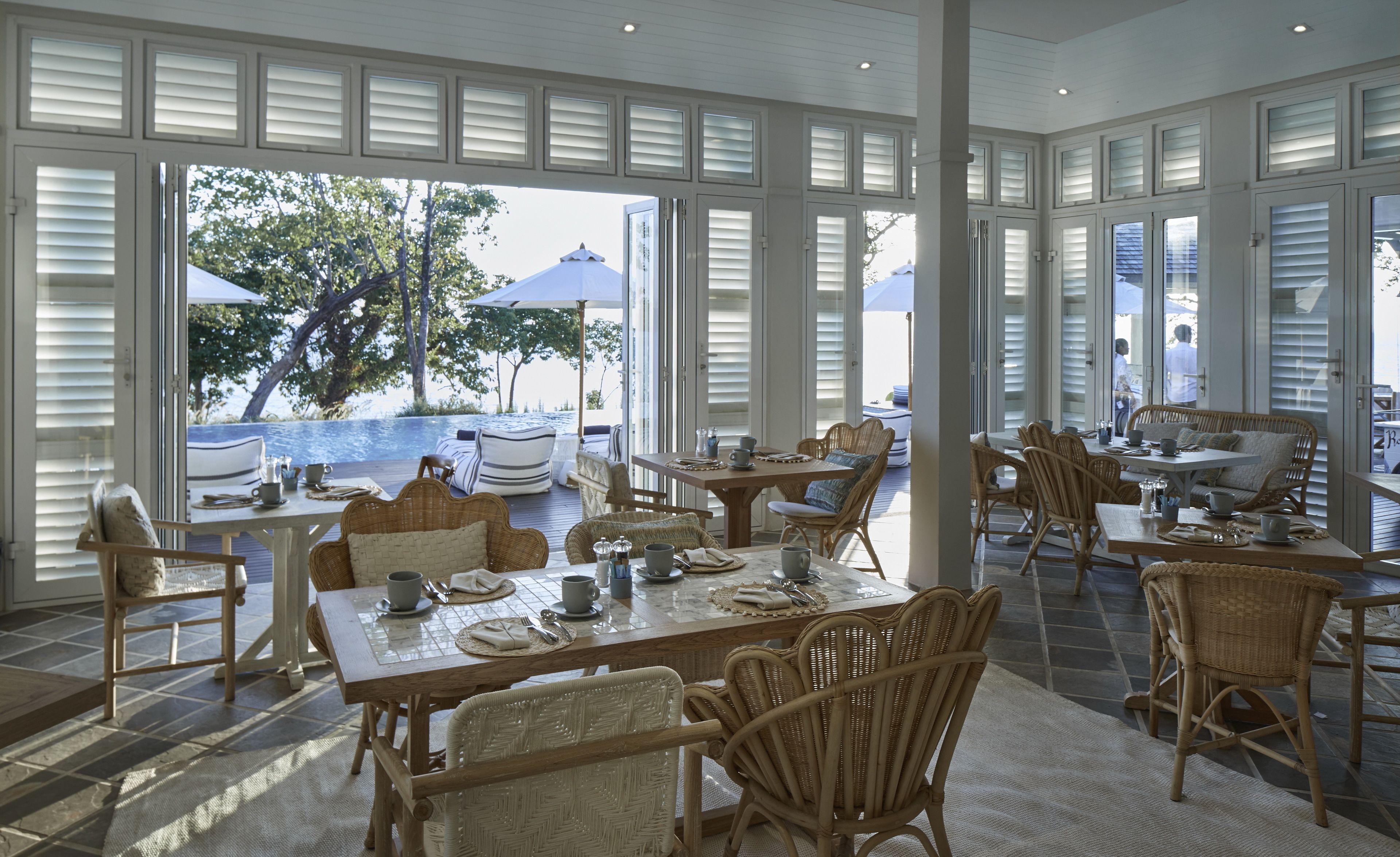 A spacious dining area with wicker furniture, large windows, and a view of the ocean.