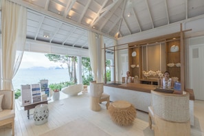 A spacious room with a wooden floor, a reception desk, and a view of the sea. - Cape Kudu Hotel (Ko Yao)