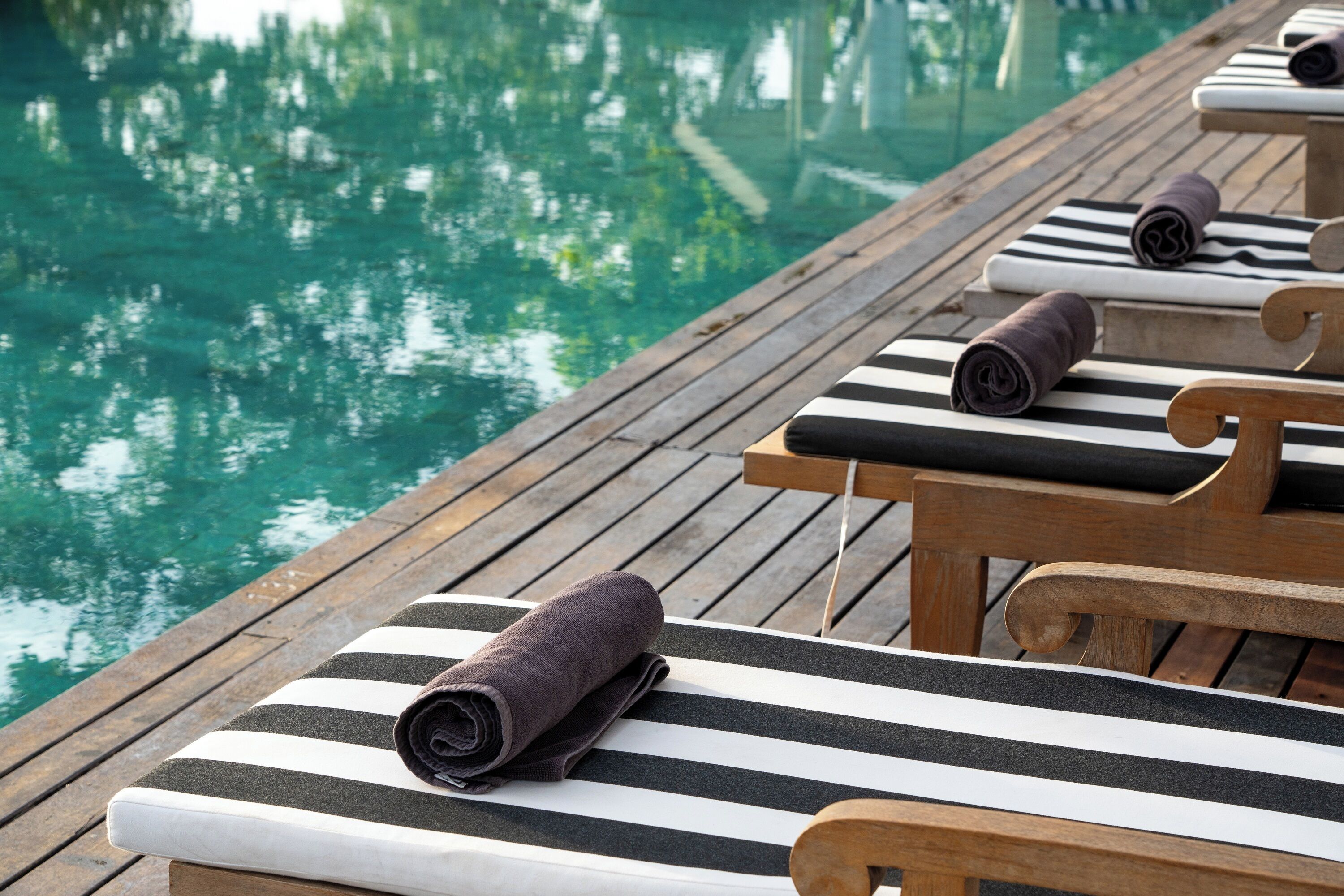 A wooden deck with striped lounge chairs and towels, overlooking a clear pool.