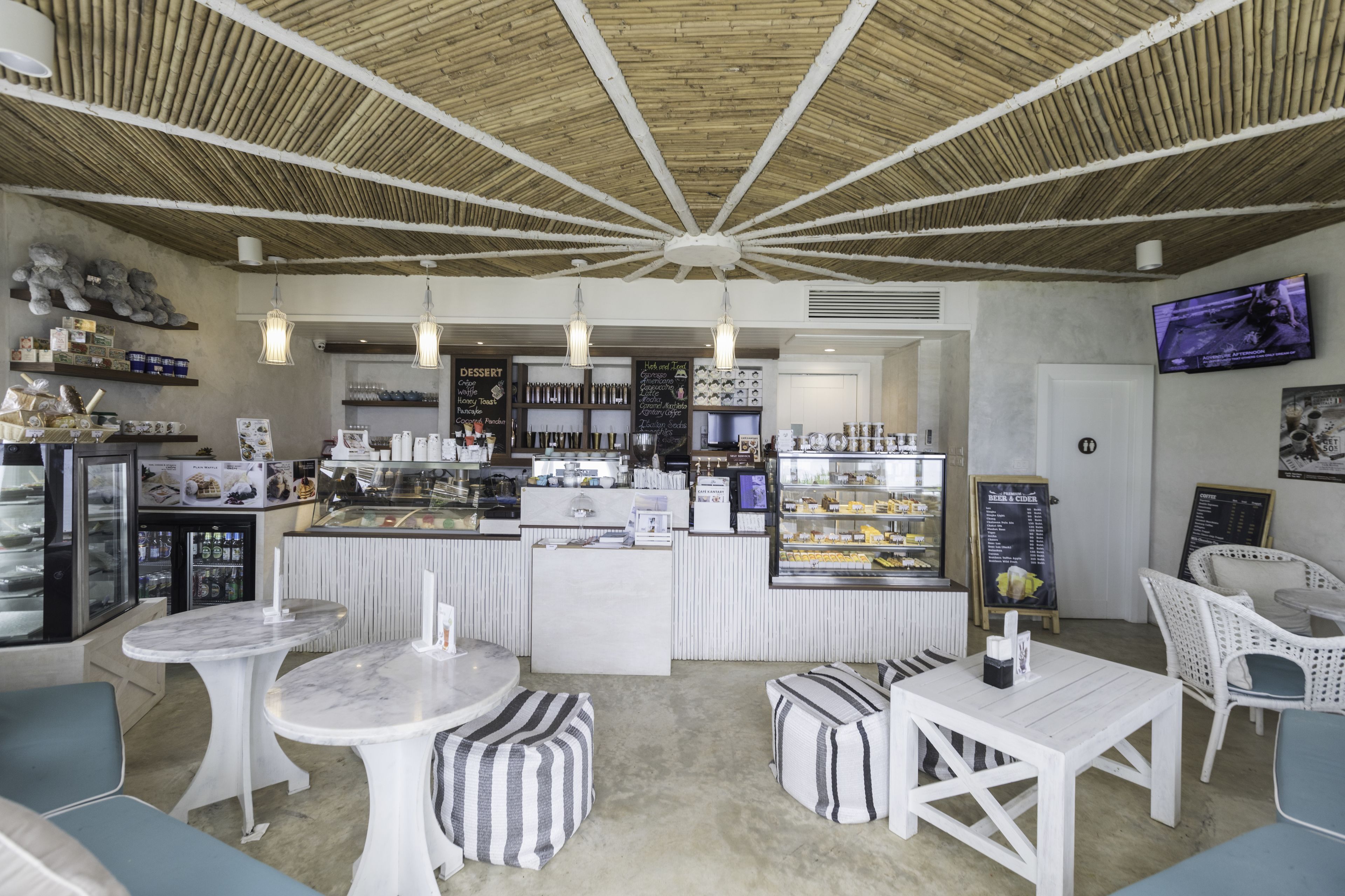 A modern cafe with a central counter, seating area, and a television screen.
