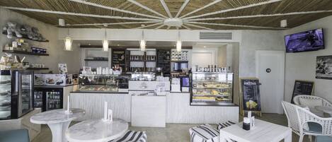 A modern cafe with a central counter, seating area, and a television screen.