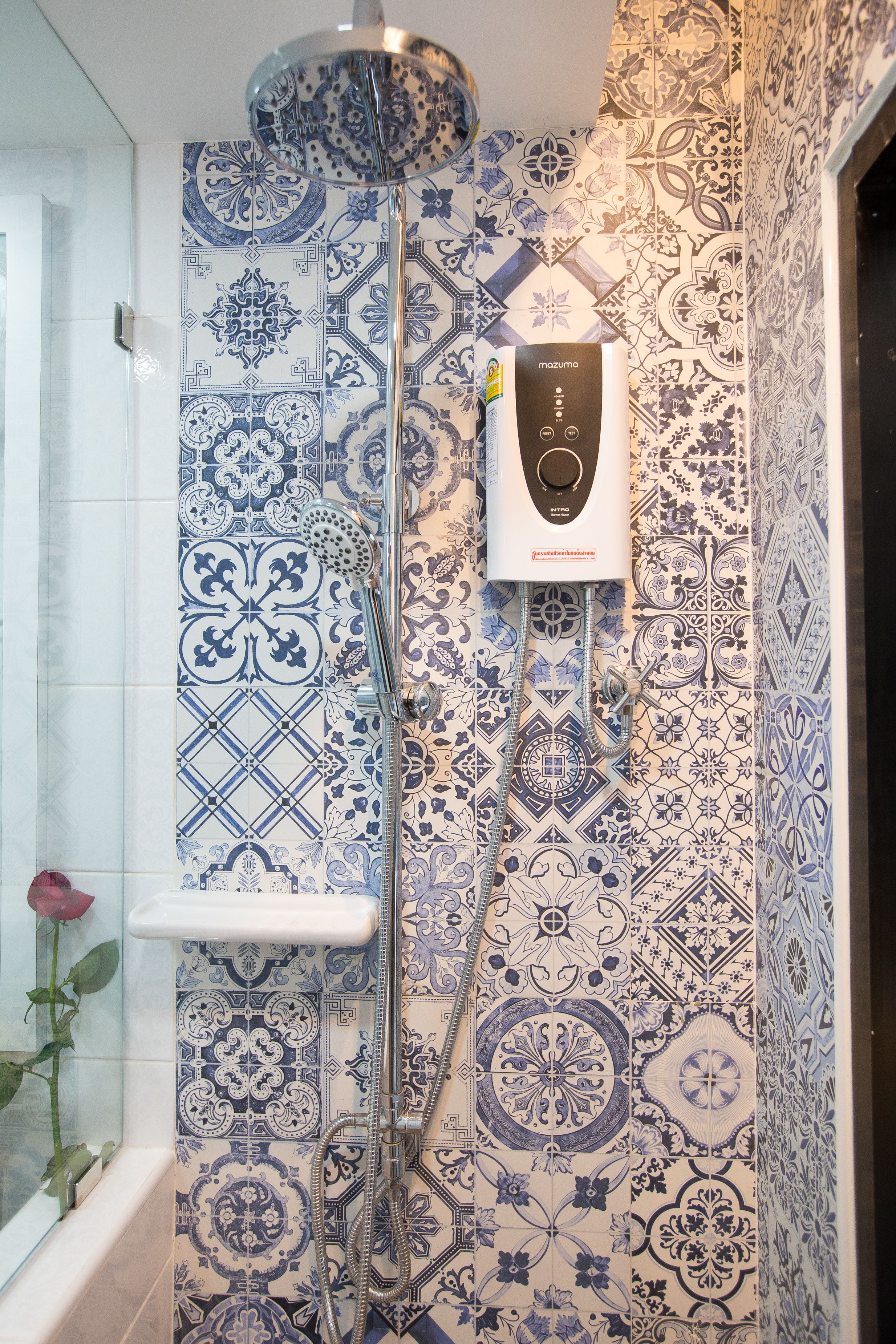 A bathroom with patterned tiles, a handheld showerhead, and a wall-mounted control panel.