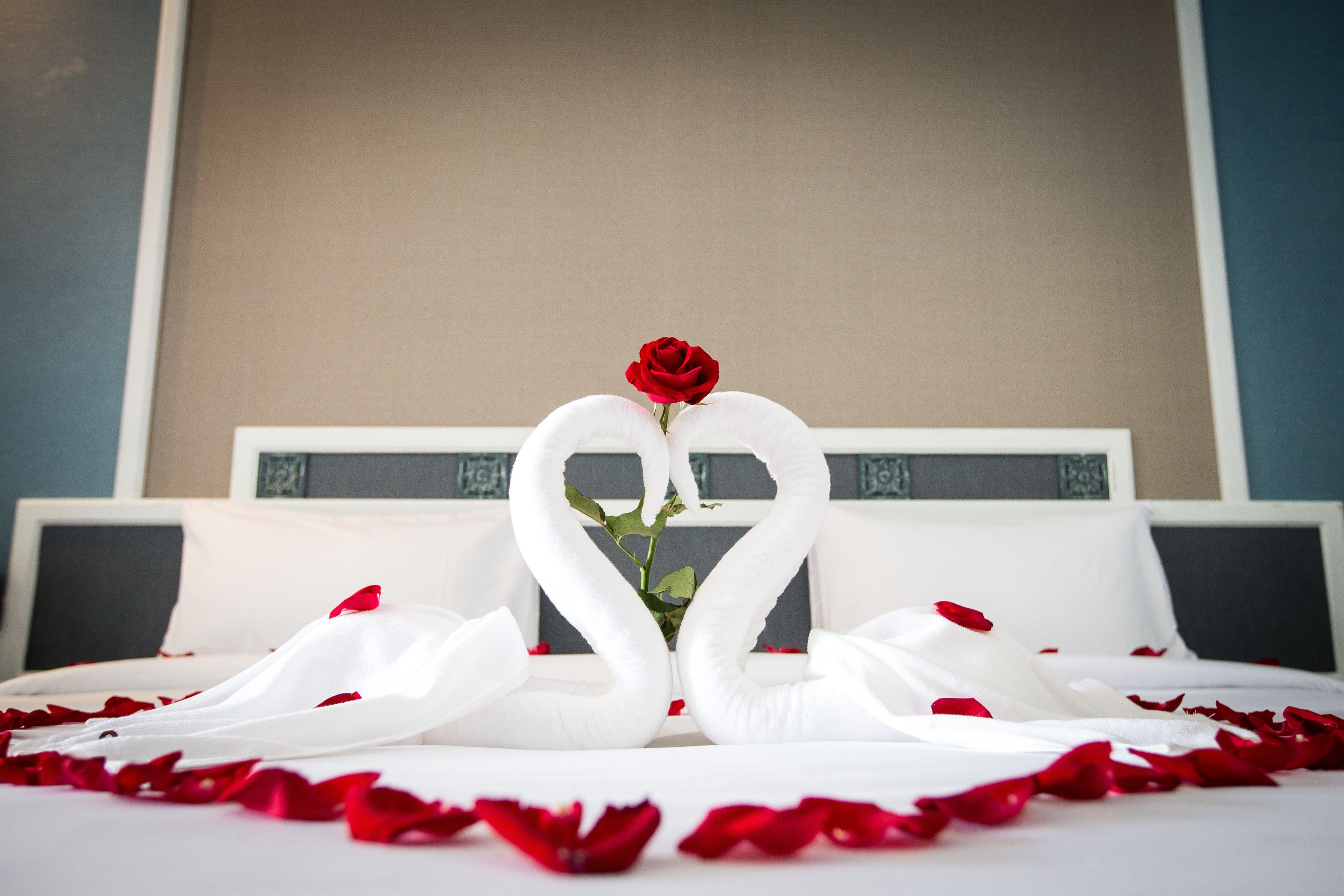 Un lit décoré de serviettes blanches disposées en forme de cœur et d’une seule rose rouge.