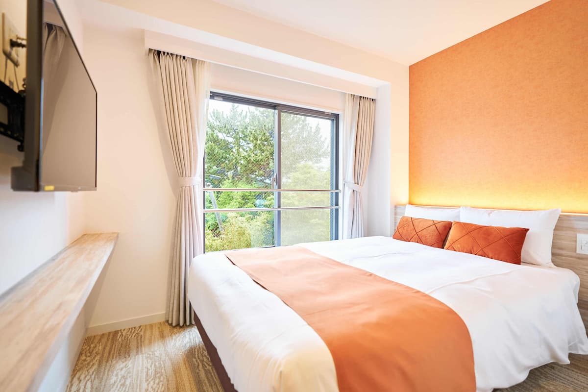 Een hotelkamer met een groot bed, een aan de muur bevestigde televisie, een raam met gordijnen en een houten vloer.