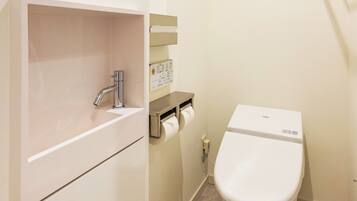 A small bathroom with a white sink, a toilet, and a paper towel dispenser.