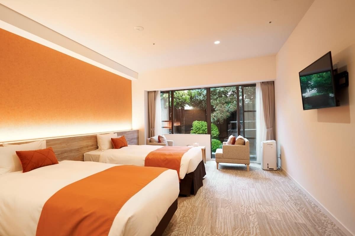 Een hotelkamer met twee bedden, een televisie en uitzicht op een tuin.