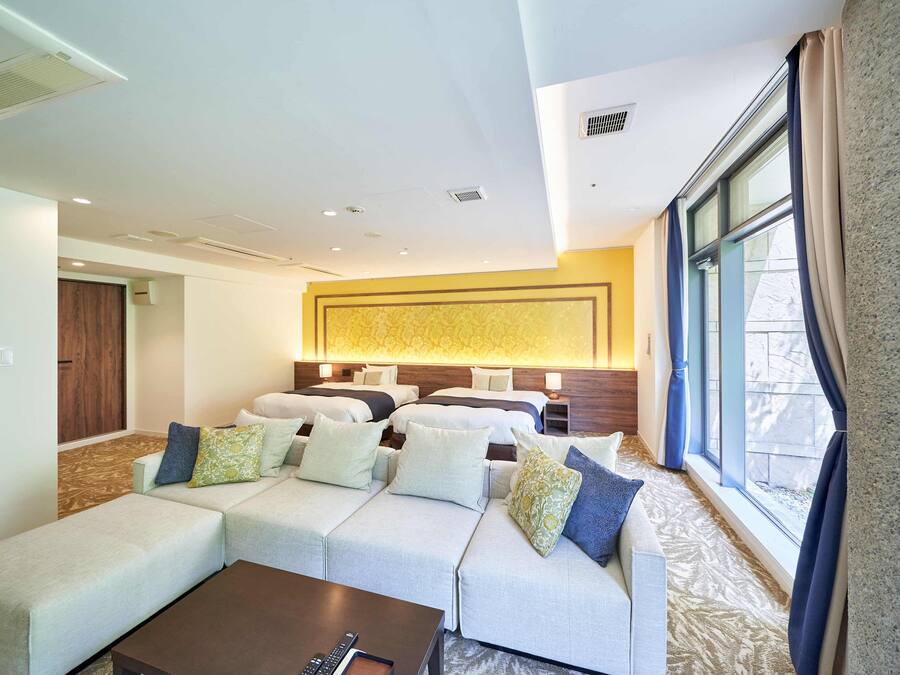 A hotel room with a large sofa set, a coffee table, and a bed with multiple pillows.