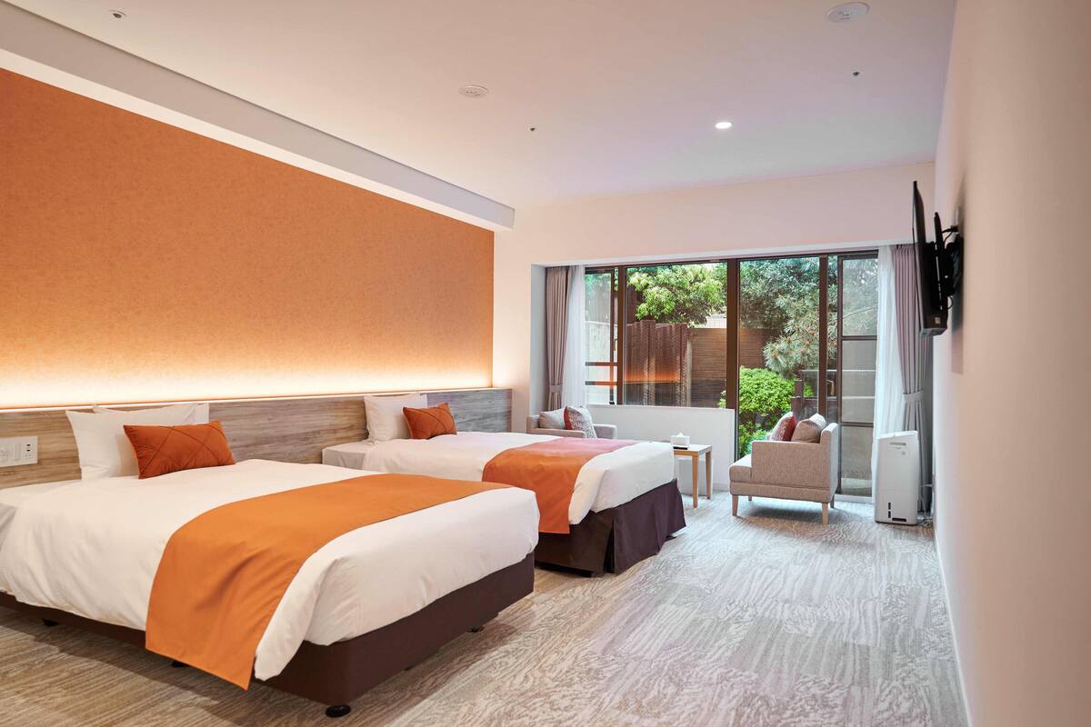 Een hotelkamer met twee bedden, een aan de muur bevestigde televisie, een tafeltje en uitzicht op het landschap door grote ramen.