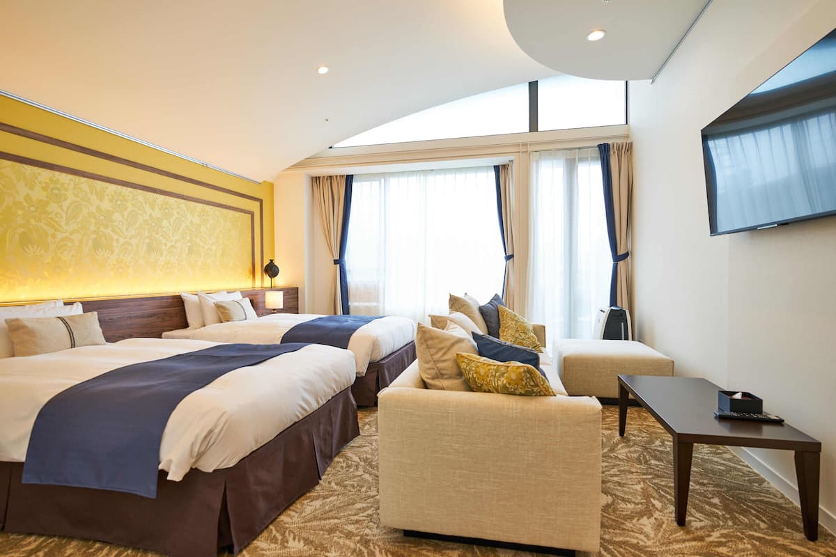 Een hotelkamer met twee bedden, een bank, een televisie en een raam met gordijnen.