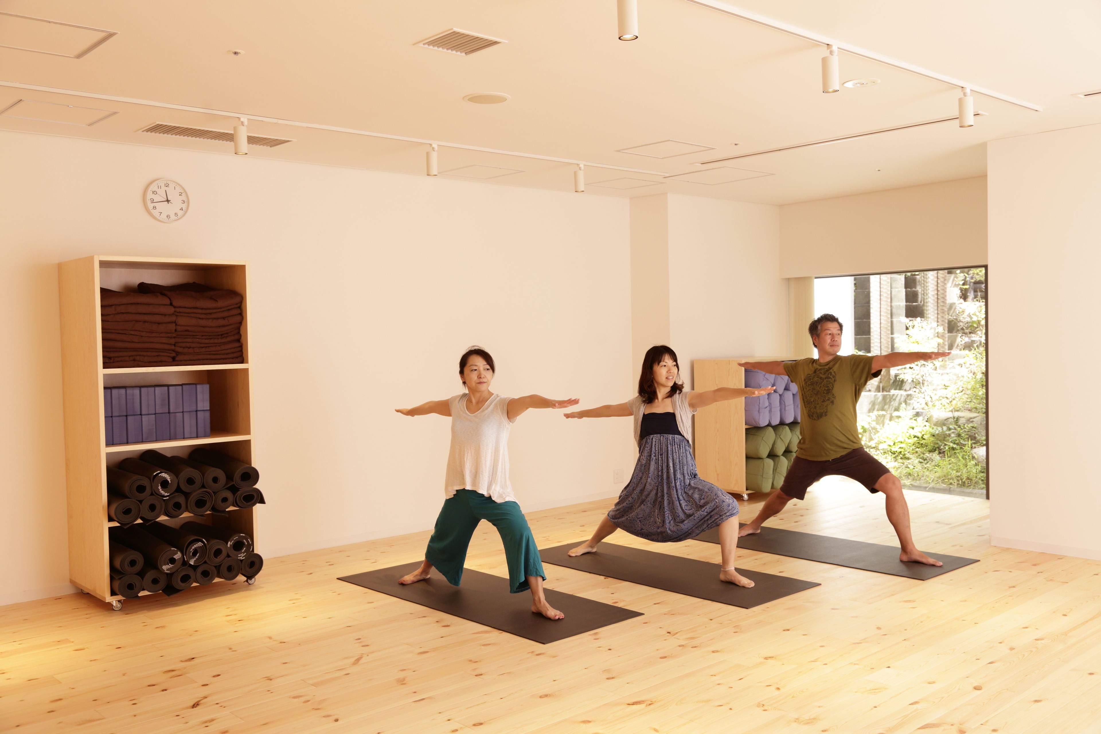 Um estúdio de yoga com piso de madeira, um relógio na parede e uma grande janela.