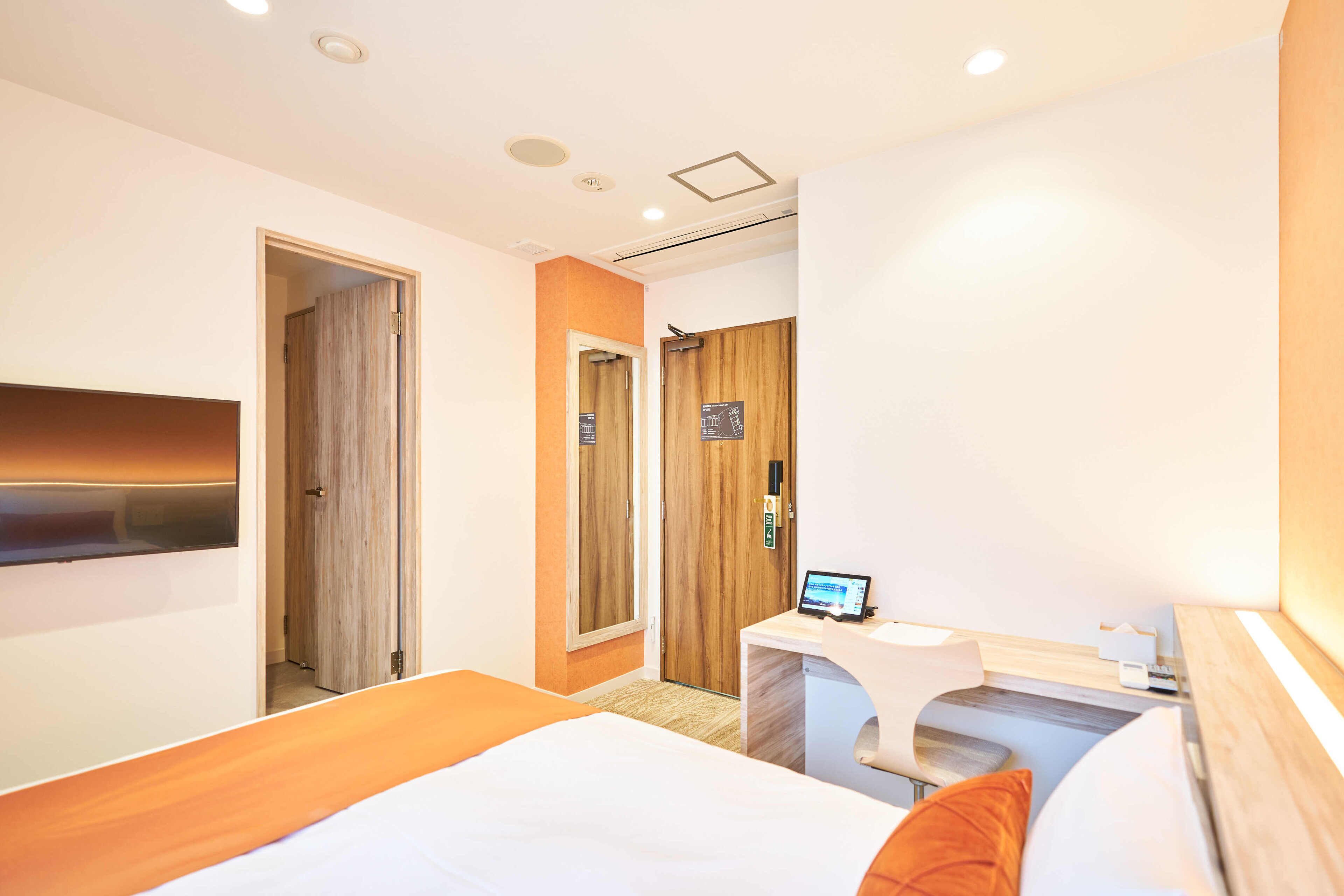 Una habitación de hotel con cama, un escritorio con ordenador y una puerta que da a otra estancia.