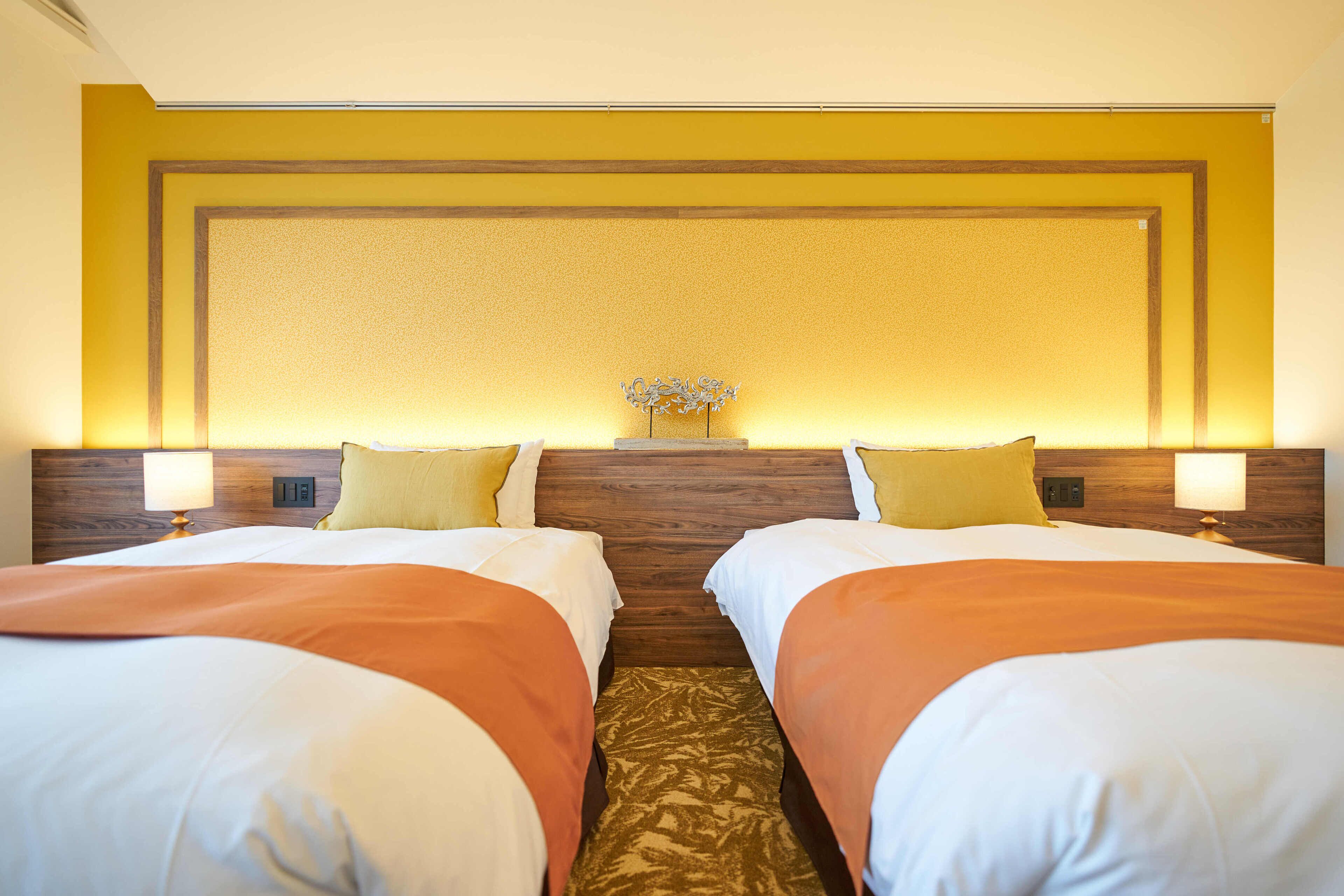 A hotel room with two beds, wooden headboard, yellow walls, and a small decorative piece on the wall.