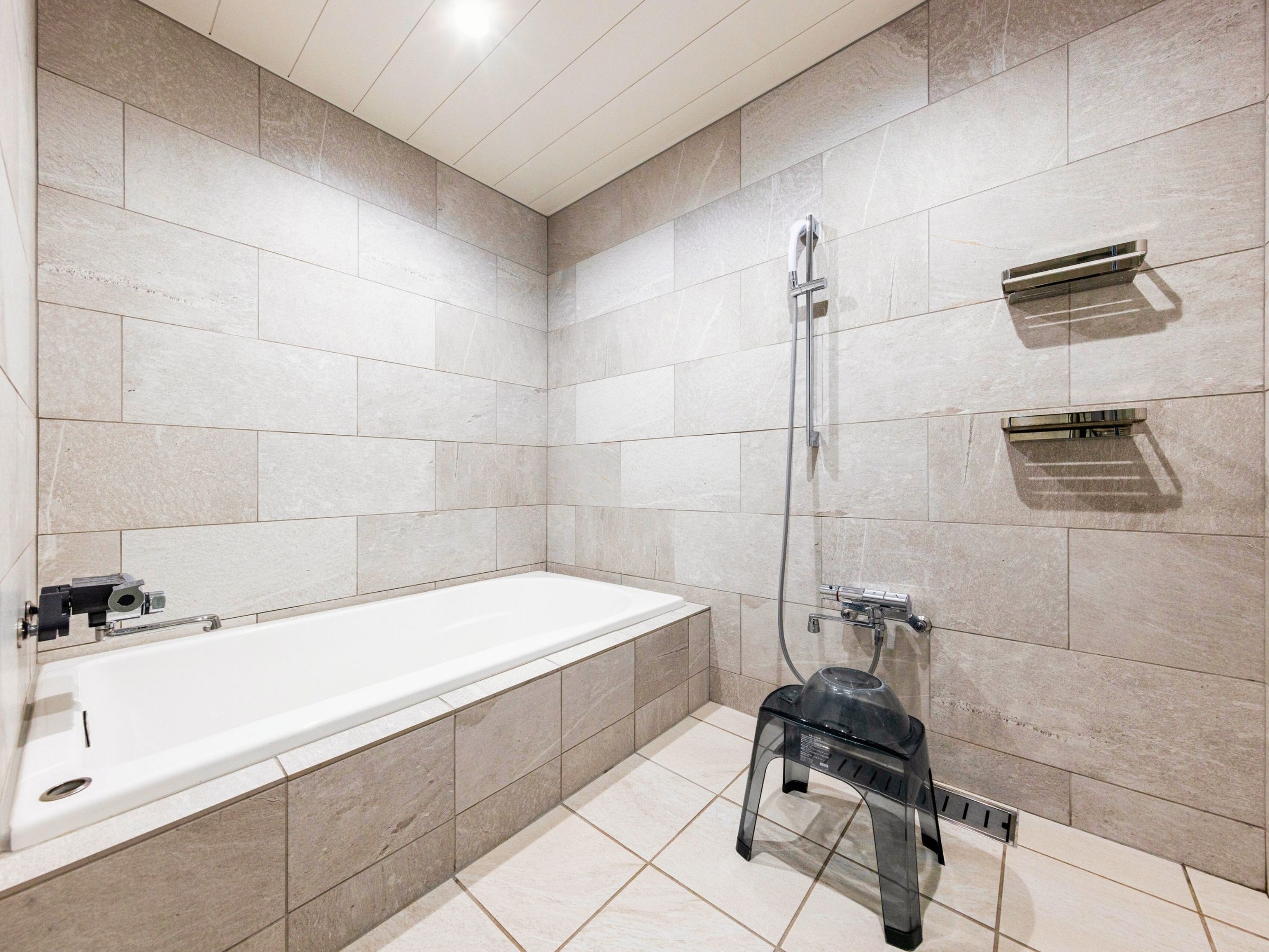Une salle de bain moderne avec une grande baignoire, une douche et un petit tabouret.