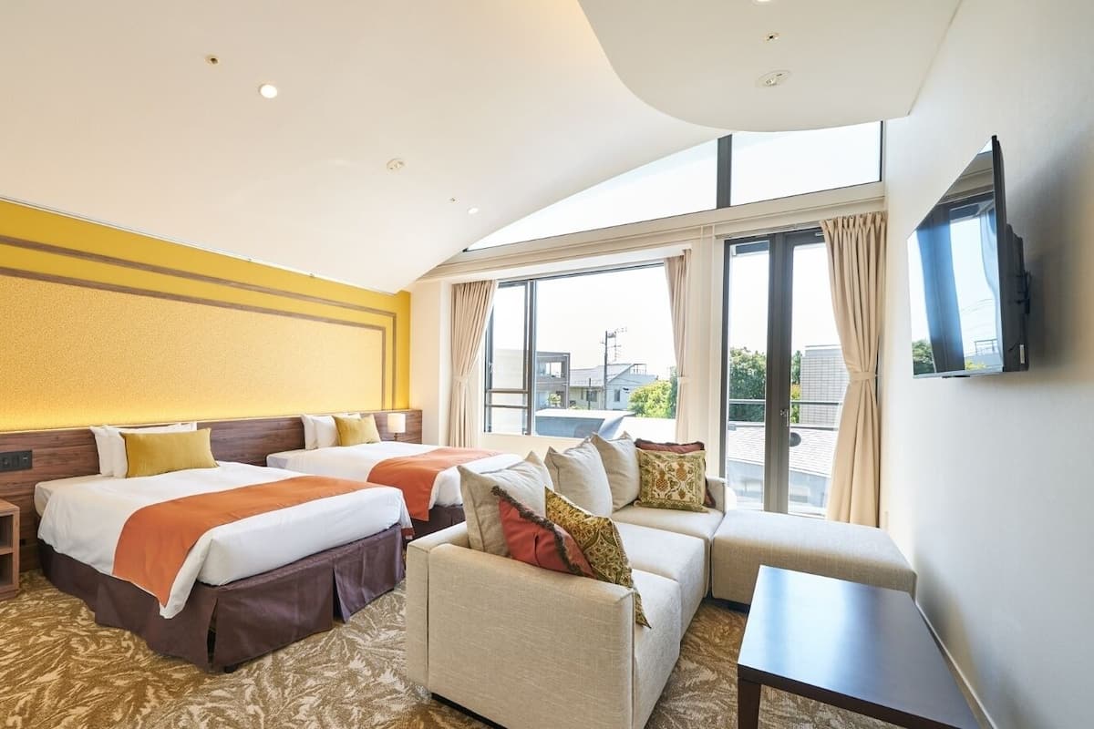 Een hotelkamer met twee bedden, een bank, een televisie en grote ramen.