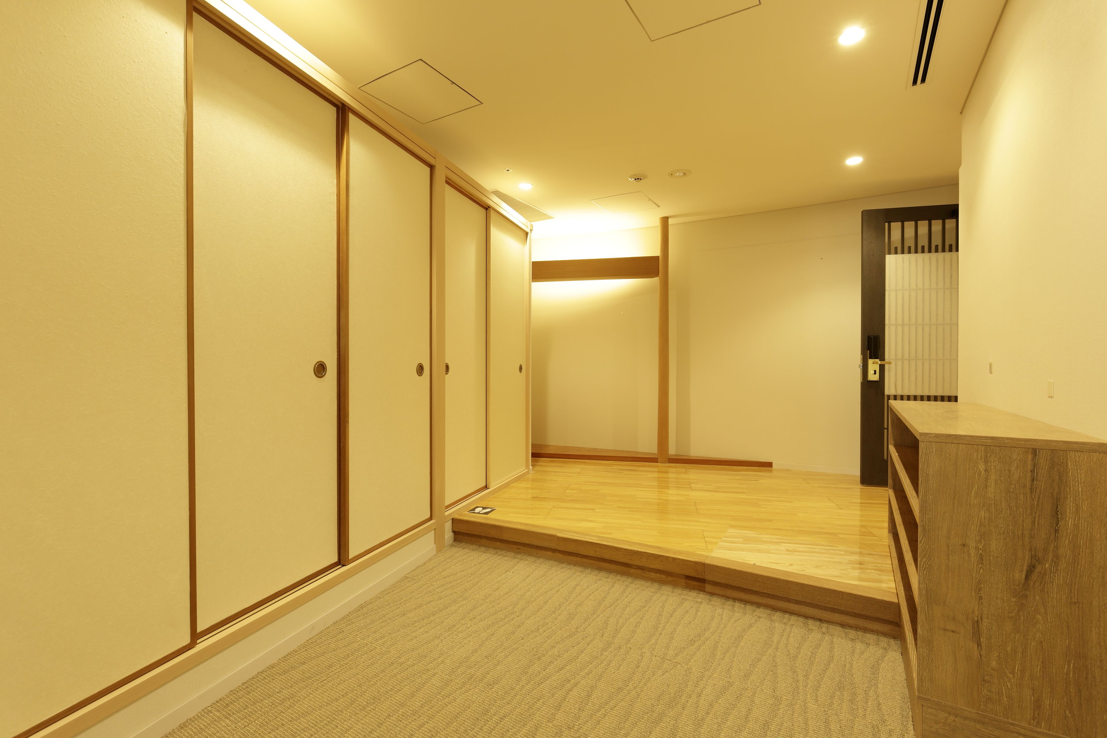 A hotel room with a wooden floor, a carpeted area, and a sliding door closet.