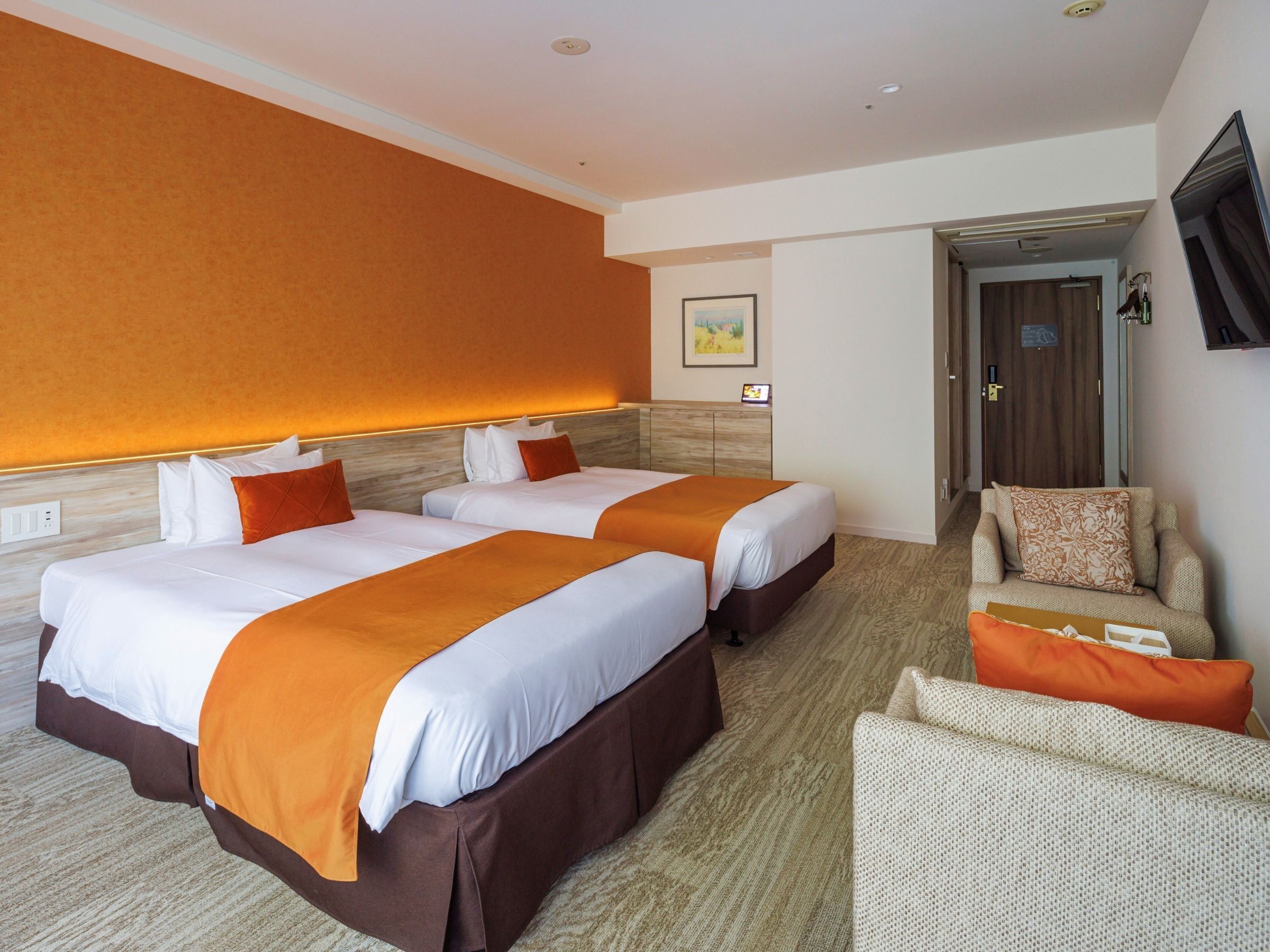 A hotel room with two beds, a sofa, and a television.