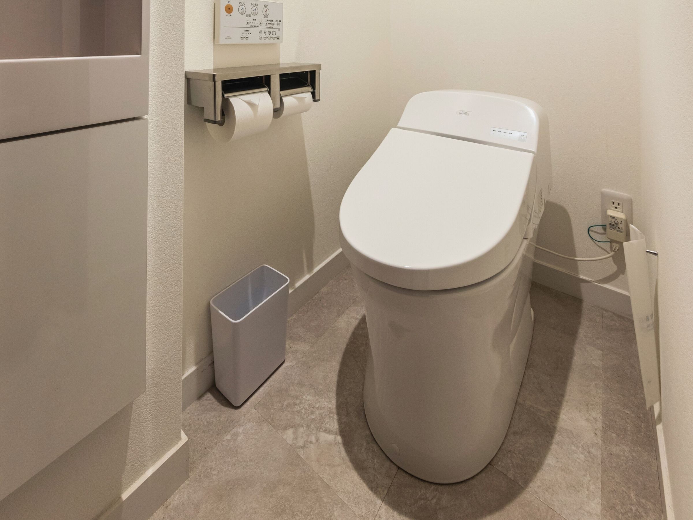 A modern bathroom with a toilet, a trash bin, and a paper towel dispenser.