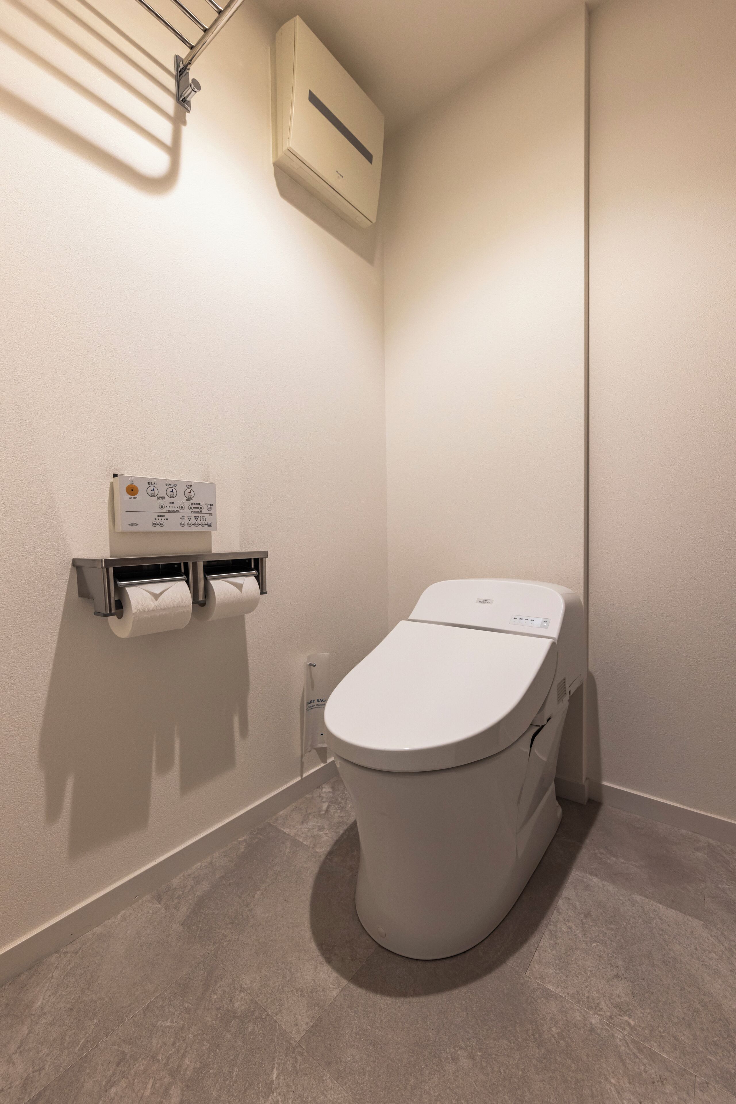 Un baño moderno con inodoro, aire acondicionado de pared y dispensador de toallas de papel.