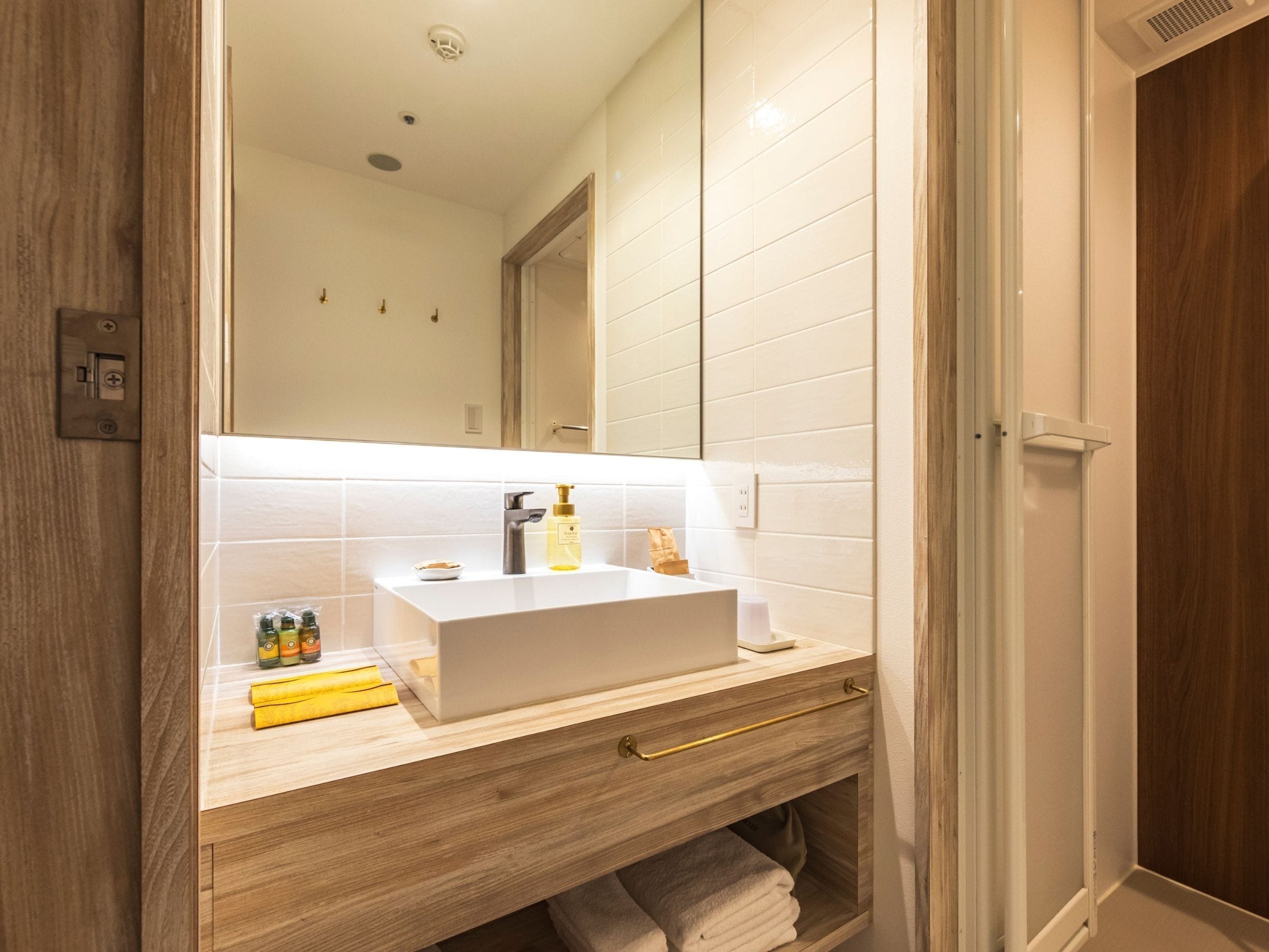 A modern bathroom with a white sink, wooden vanity, and a large mirror.