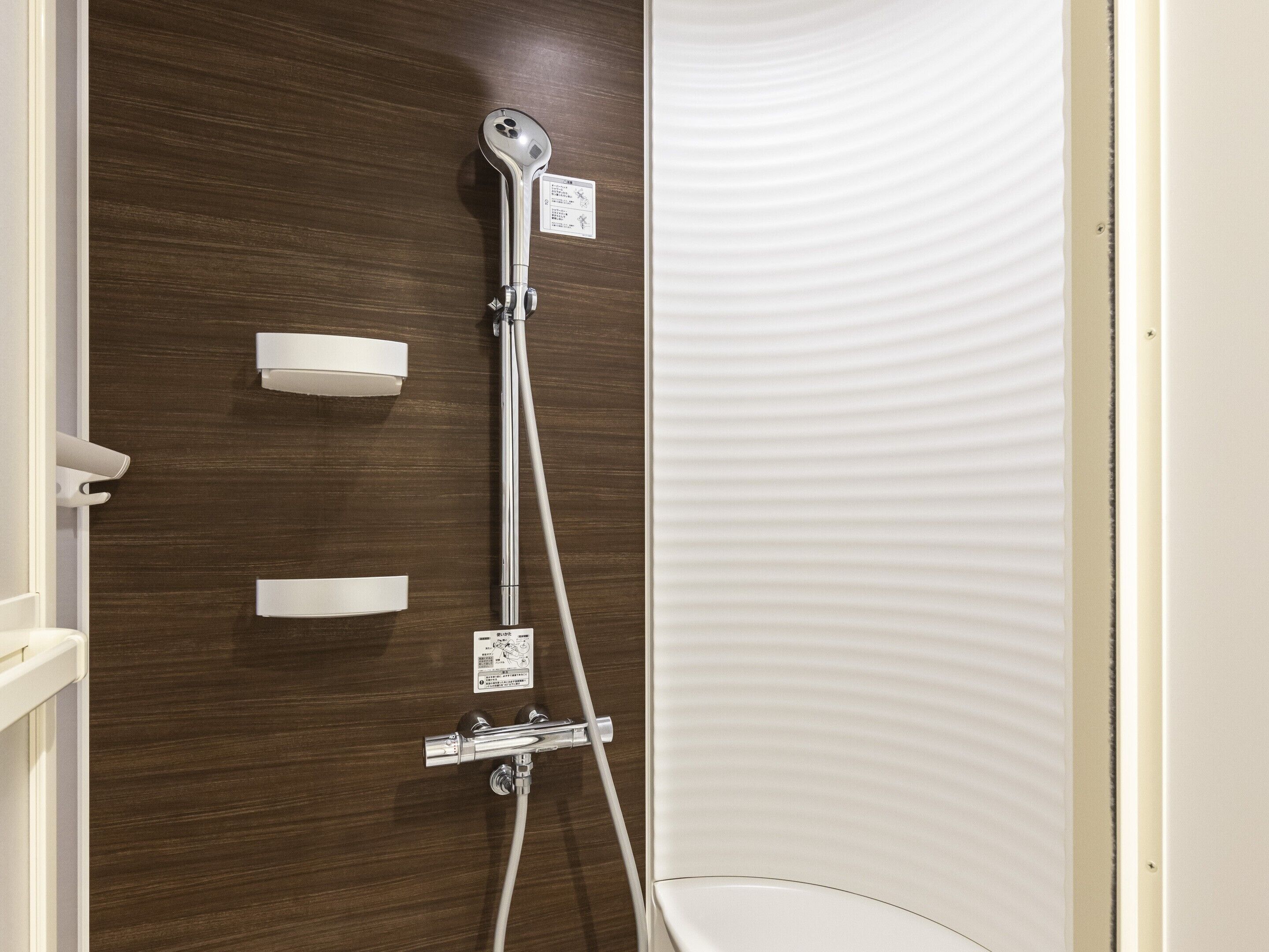 A shower with a control panel and a white textured wall.