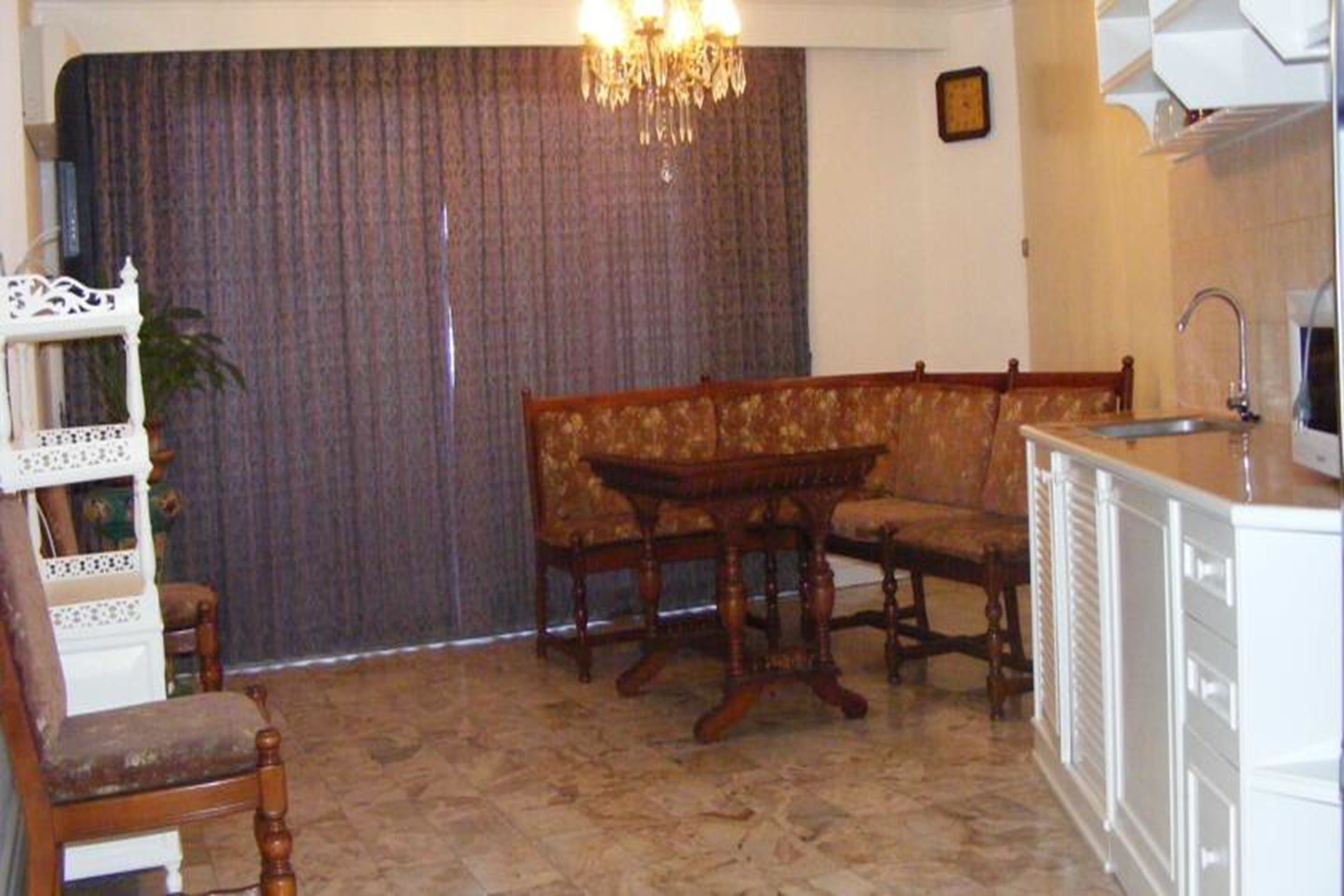 Een woonkamer met een bank, een houten tafel, een kroonluchter en een keuken met een spoelbak en kastjes.
