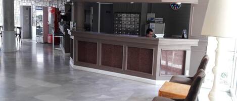 Un vestíbulo de hotel con una recepción, zona de estar y una máquina expendedora.