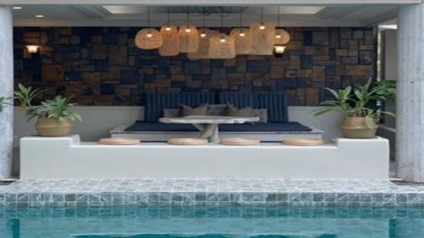 Zona de piscina con mobiliario, pared de piedra e iluminación colgante.