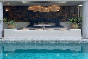 A poolside area with a seating arrangement, a stone wall, and hanging lights. - Garden Paradise Hotel & Serviced Apartment (Pattaya)