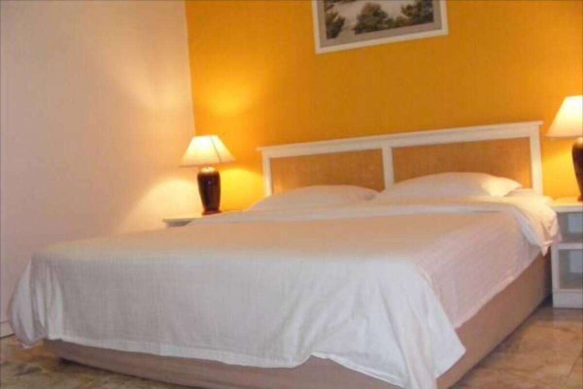 Una cama con ropa de cama blanca en una habitación con paredes amarillas y suelo de mármol.