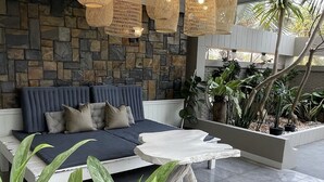 Un área de estar moderna al aire libre con un muro de piedra de fondo, un sofá azul y lámparas colgantes tejidas.