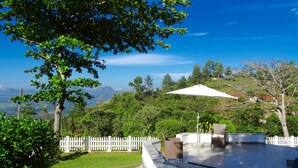 Un espace patio aménagé avec du mobilier d’extérieur, une clôture blanche et une vue sur un paysage montagneux.