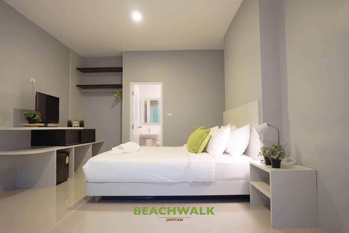 A modern bedroom with a bed, bedside tables, a TV, and a bathroom visible through an open door.
