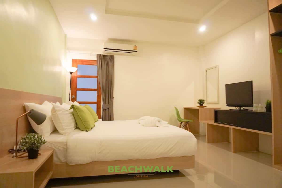 A hotel room with a bed, a TV, an air conditioner, a desk, and a chair.