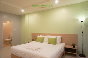 A hotel room with a bed, a bedside table, a nightstand, a floor lamp, and a small plant. - Beachwalk Jomtien (Pattaya)