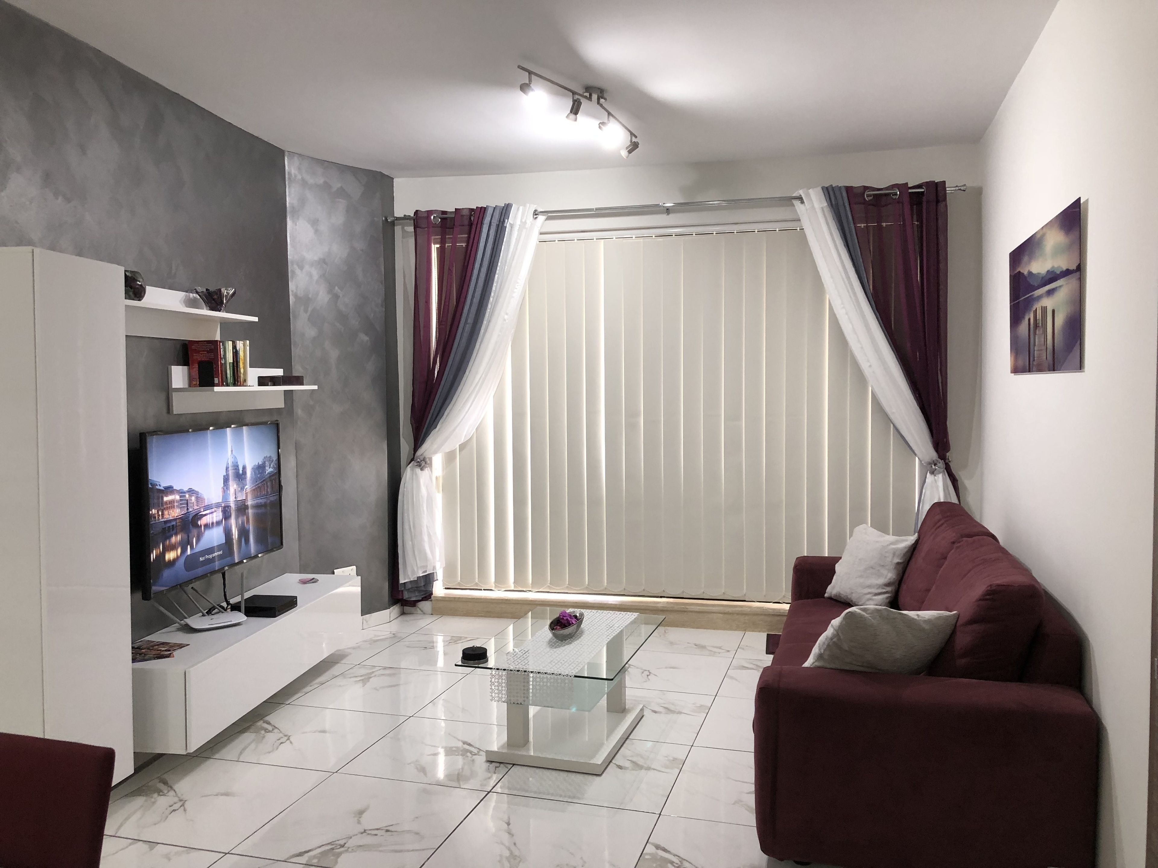 Een moderne woonkamer met een flatscreen televisie, een witte bank, een glazen salontafel en een marmeren vloer.