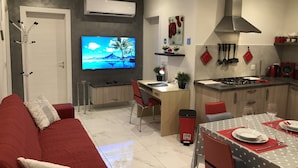 A modern kitchen with a dining area, a TV mounted on the wall, and a red sofa in the living area. - Marsascala Sea View Luxury Apartment & Penthouse (Marsaskala)