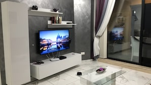 A modern living room with a flat-screen TV, white entertainment unit, glass coffee table, and a sliding glass door leading to a balcony. - Marsascala Sea View Luxury Apartment & Penthouse (Marsaskala)