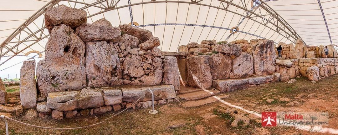 Des ruines anciennes en pierre, situées sous une vaste structure arquée.