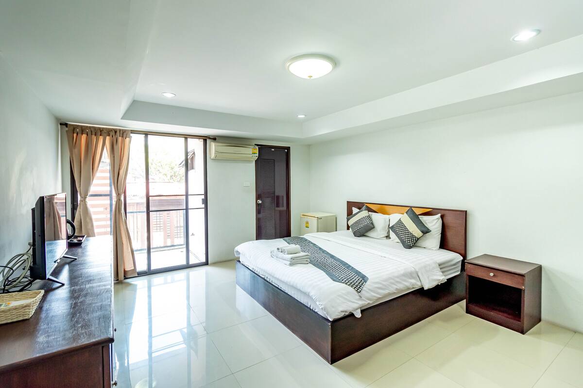 A modern bedroom with a large bed, a desk, and a sliding glass door leading to an outdoor area.