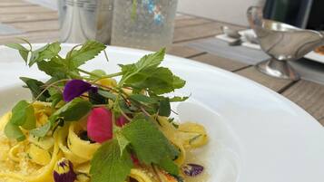 En anretning med pasta og grønt, et glas drik og en potteplante i baggrunden.